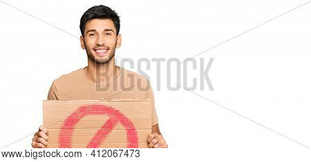 Young handsome man holding prohibited warning banner looking positive and happy standing and smiling with a confident smile showing teeth 