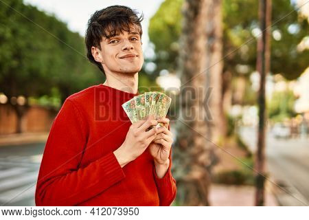 Young hispanic man smiling happy holding argentinian pesos banknotes at the city
