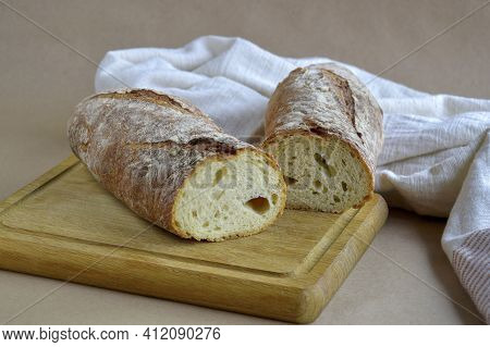 Bread Loaf, Cut Into Two Pieces, On Wooden Cutting Board. Baked Bread And Dish Towel On Craft Paper,