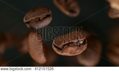 Falling Roasted Coffee Beans on Brown Background, macro shot, close-up.