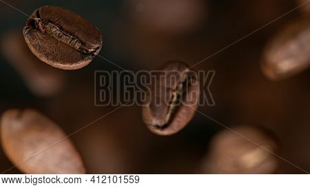 Falling Roasted Coffee Beans on Brown Background, macro shot, close-up.