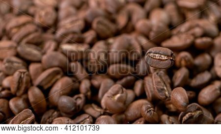 Falling Roasted Coffee Beans on Brown Background, close-up.