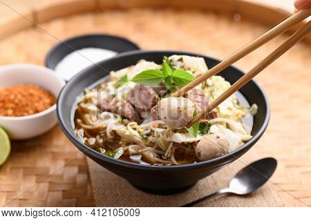 Hand Holding Chopsticks And Eating Rice Noodle Soup With Pork, Pork Ball And Vegetables In A Bowl, T
