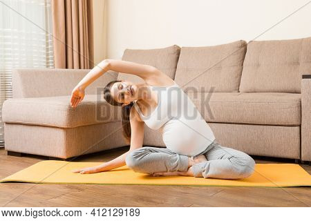 Beautiful Young Pregnant Woman Sitting Near Sofa In Yoga Pose At The Home. Pregnancy Yoga And Fitnes