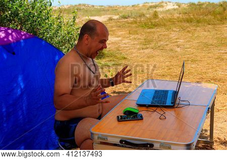 Man Using His Laptop Sitting At A Folding Picnic Table In A Camping. Working While Traveling. Freela
