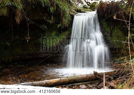 A waterfall cascades into a woodland glade in Maspie Den, Falkland, Fife during a winter morning