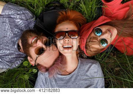Top View Of A Smiling Young People In Sunglasses, Lying Down On A Green Grass, In The Park, Wear Sun