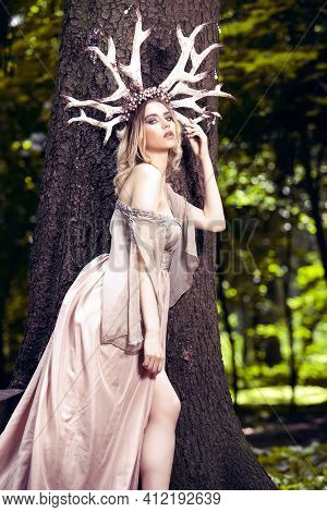 Portrait Of Passionate Sexy Caucasian Girl Posing With Artistic Deer Horns And Long Light Dress In S