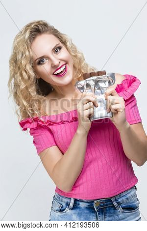 Portrait Of Positive Smiling Caucasian Blond Girl With Unwrapped Bar Of Chocolate Posing On White. V