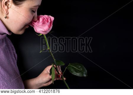 Fat Young Woman Sniffing Pink Rose On Black Background With Copy Space.