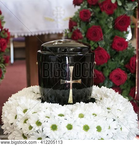 Black Urn On The Funeral Day In Church; Surrounded With Daisies And Roses