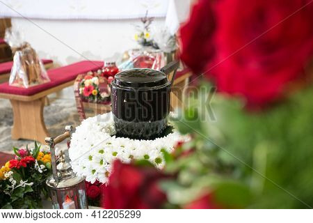 Black Urn On The Funeral Day In Church; Surrounded With Daisies And Roses