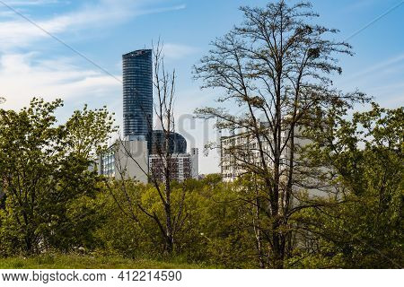 Wroclaw, Poland - May 8 2020: Top Of Sky Tower Skyscraper Behind Bushes Trees And Buildings