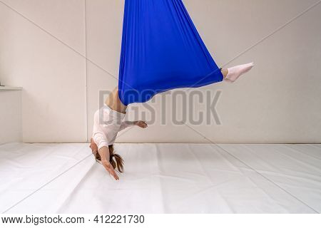 A Young Woman Poses While Doing Anti-gravity Aerial Yoga In A Blue Hammock On A White Background.