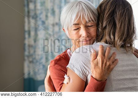 Close up of senior mother embracing adult daughter after covid-19 vaccination shot. Happy old grandmother and granddaughter meeting each other at the injection of the covid19 vaccine from virus.