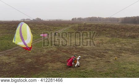 Beginning Of Paragliding, Instructor With A Red Superman Cloak And Client Starting To Fly. Action. P
