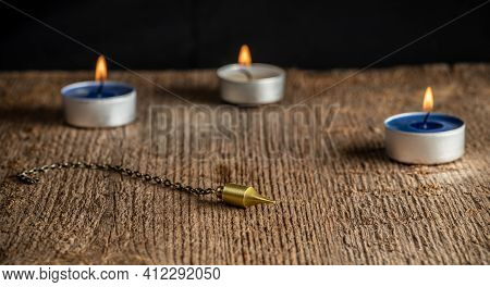 The Pendulum On A Chain With A Natural Crystal On A Background Of Wood Texture With Three Burning Ca