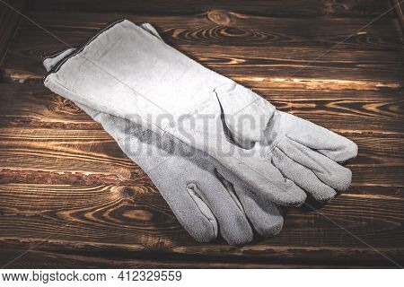 White Leather Welder Gloves On A Wooden Background. A Studio Photo With Hard Lighting.