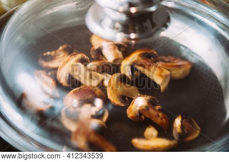 Defocused View Of Frying Pan Covered With Glass Lid Of Fresh Mushrooms Being Fried
