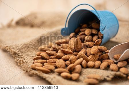 Almonds Pour From Blue Bucket
 On Wooden Table. Almond Concept With Copyspace.