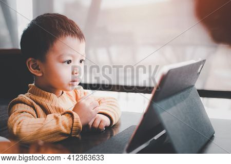 Asian Boy Looking At The Tablet Screen Attentively. Overstimulated Children Concept. Too Much Screen