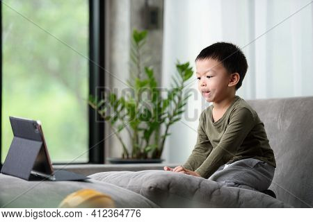 Asian Boy Looking At The Tablet Screen Attentively. Overstimulated Children Concept. Too Much Screen