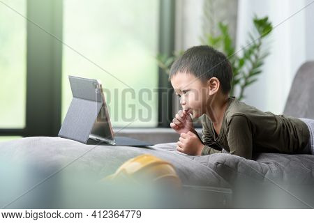 Asian Boy Looking At The Tablet Screen Attentively. Overstimulated Children Concept. Too Much Screen