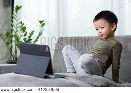 Asian Boy Looking At The Tablet Screen Attentively. Overstimulated Children Concept. Too Much Screen