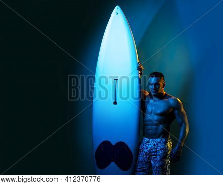 Sexy Man With Serf Board. Male Serfer With Fit And Firm Body. Neon Surfboard Light Background