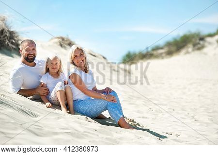 A Family Of Three Sit On The Sand Dunes Near The Town Of Nida.lithuania.