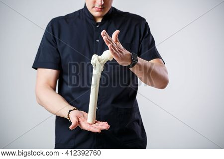 Young Male Doctor Chief Physician In A Black Surgical Suit. Close-up Portrait. Holds A Femur In His