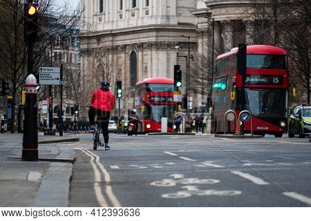 Cyclist Wearing A Red Jacket Waiting For The Traffic Lights On An Intersection, Two Double Decker Bu