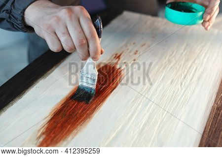 A Working Cabinetmaker Holds A Brush In His Hand And Paints A Wooden Surface. A Trace Of Paint On A 
