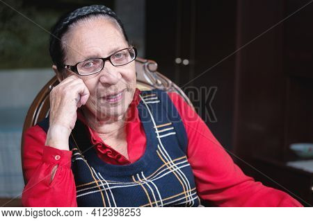 Portrait Of An Attractive Smiling Old Woman Sitting On An Armchair At Home. Happy Old Age