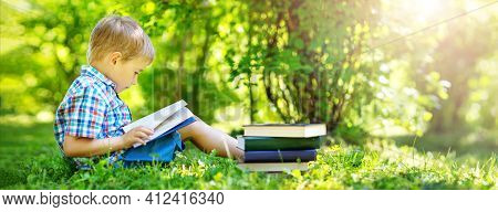 Five Years Old Child Sitting On The Grass And Reading A Book