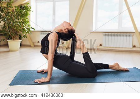 Young Woman In Black Sportswear, Practicing Yoga, Performs An Exercise With A Dog Facing Up With A R