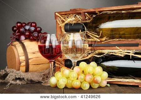 Case in legno con bottiglie di vino, botte, bicchiere da vino e dell'uva sul tavolo di legno su sfondo grigio