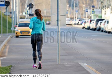 Slim Girl Running On The Sidewalk Along The City Street, Rear View. Alone Runner, Concept Of Workout