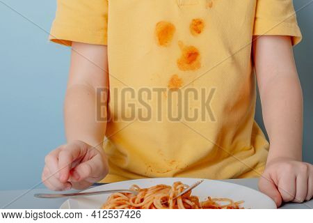 Cute Boy Eating Spaghetti Bolognese At Home. Concept Of Dirty Stains On Clothes. Isolated On Blue Ba