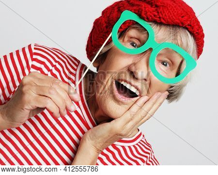 lifestyle, people and party concept: funny grandmother wearing red clothes holding falce glasses and  ready for party