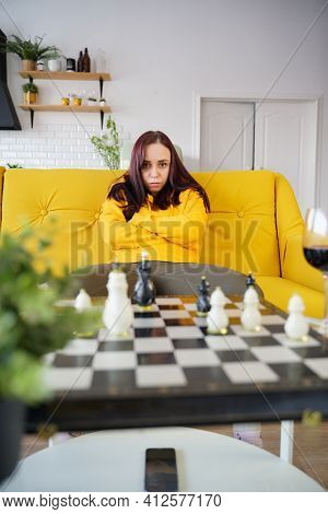 Young Upset Woman Playing Chess Sitting On Sofa. Distressed Female Plays In Logical Board Game With
