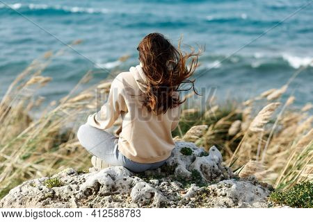 Young Yoga Woman Meditation, Mindfulness On Seaside Rock Cliff Edge. Beautiful Sea View. Windy Wheat