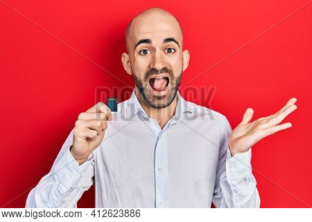 Young bald man holding sdxc card celebrating achievement with happy smile and winner expression with raised hand 