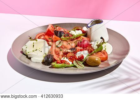 Tomato, olives and mozzarella salad . Restaurant appetizer plate on white table with pink wall. Day sunlight with hard shadow of fern palm leaves. Summer or spring restaurant food concept