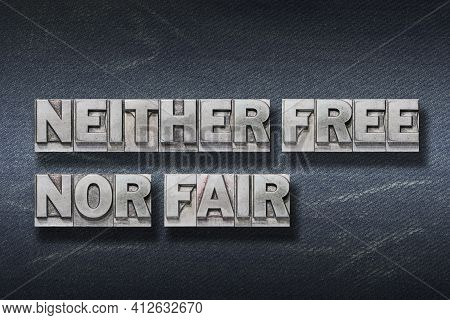 Neither Free Nor Fair Phrase Made From Metallic Letterpress On Dark Jeans Background