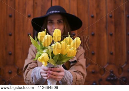 Beautiful Young Girl In A Hat With A Big Bouquet Of Yellow Tulips. Walks Around The Old Town In Euro