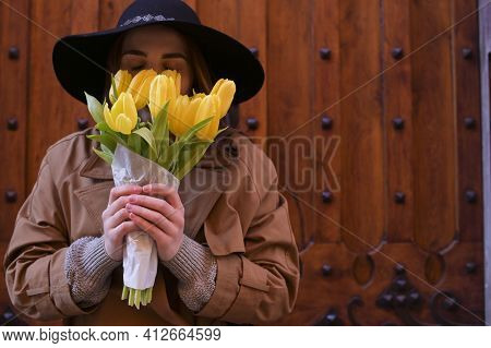 Beautiful Young Girl In A Hat With A Big Bouquet Of Yellow Tulips. Walks Around The Old Town In Euro