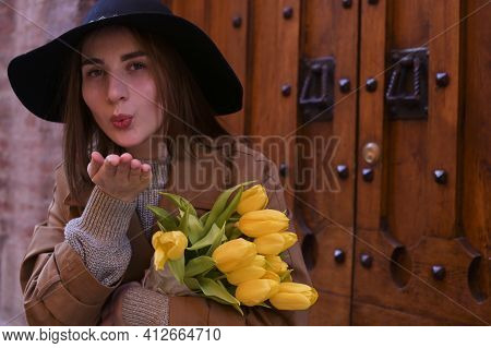 Beautiful Young Girl In A Hat With A Big Bouquet Of Yellow Tulips. Walks Around The Old Town In Euro