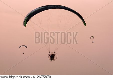 Silhouette Of The Paramotor Gliding And Flying In The Air Through Soft Sunlight Sky