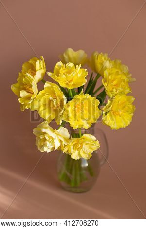 Yellow Tulips In Glass Vase On Beige Background.